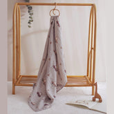 Muslin baby swaddle with Cars print hanging from wooden peg near crib